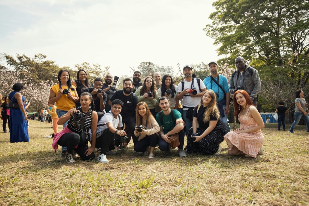 A diverse group of photographers poses with cameras in a sunny park setting. Instagram