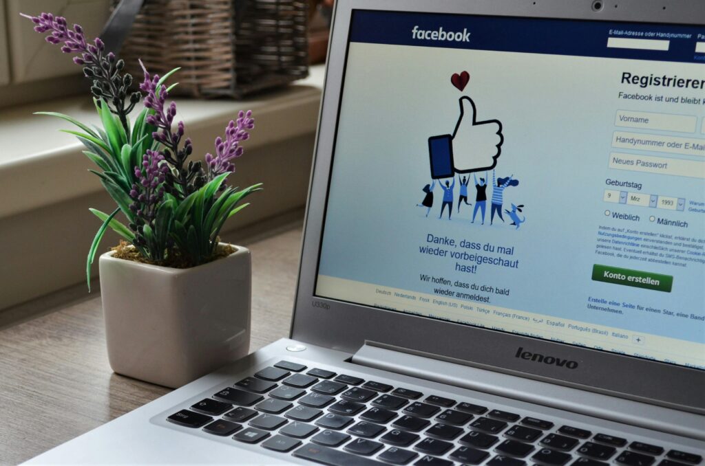A Lenovo laptop displaying Facebook login beside a lavender plant indoors. Facebook